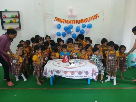 Children gathered around a birthday cake with balloons and a banner behind them